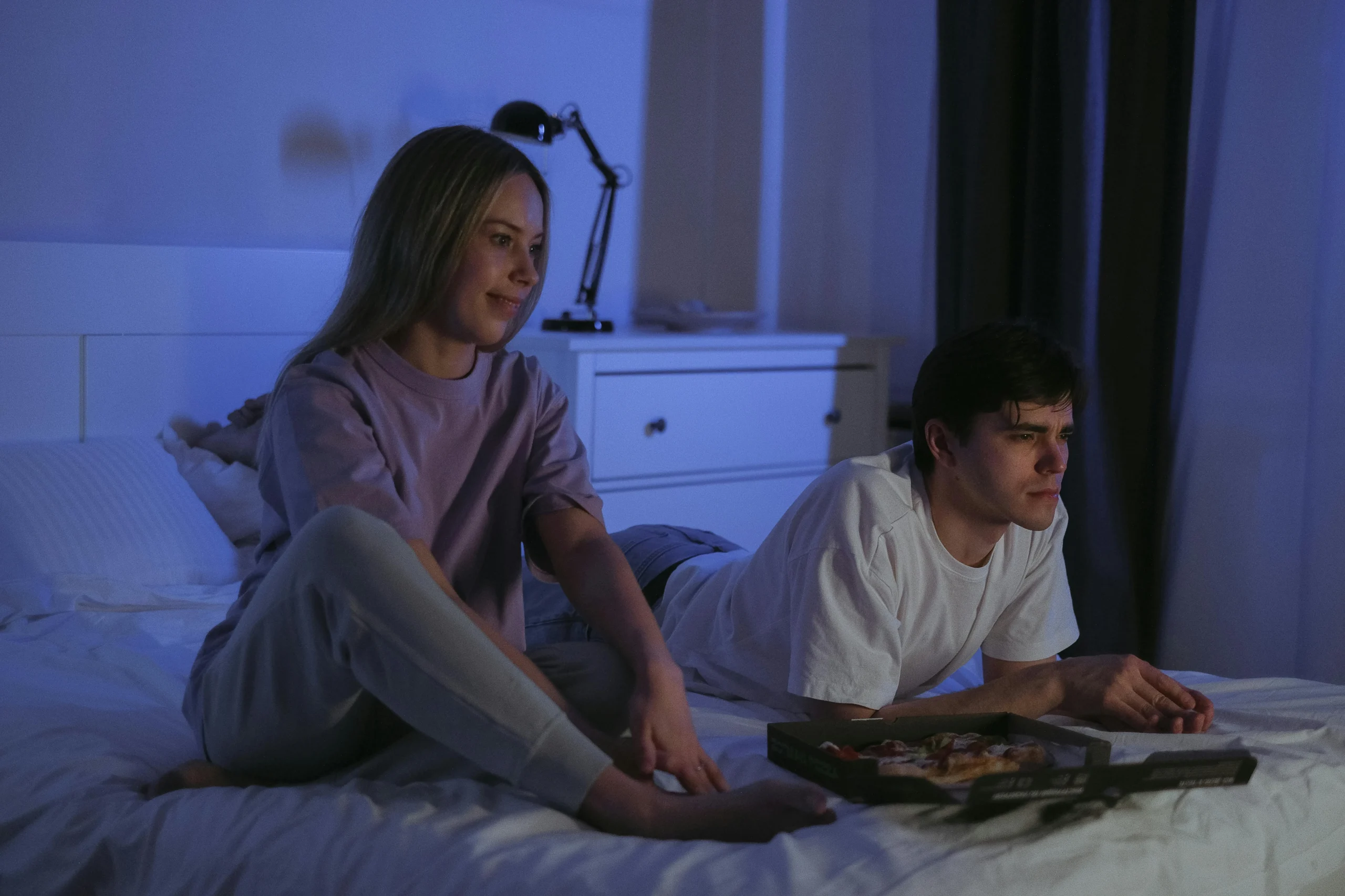Couple regardant un film au lit le soir, part de pizza à côté